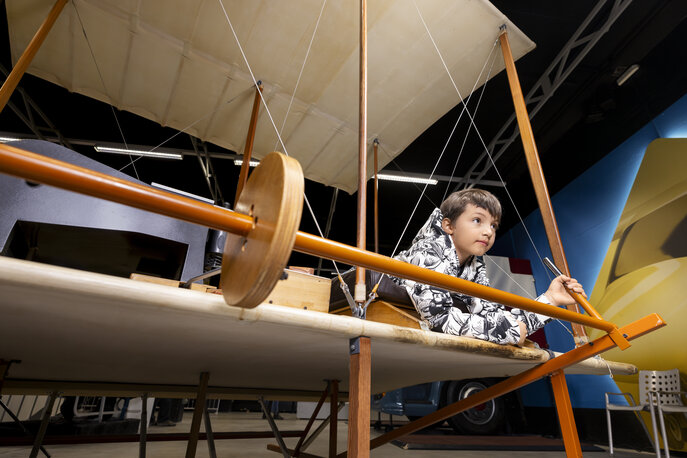 Ein 10 jähriger Junge liegt auf einem Doppeldecker Flugsimulator und steuert den Simulator.