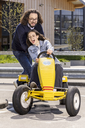 Ein Mann mit schwarzen langen Locken stösst ein Mädchen im Alter von 15 Jahren auf einem GoKart. 