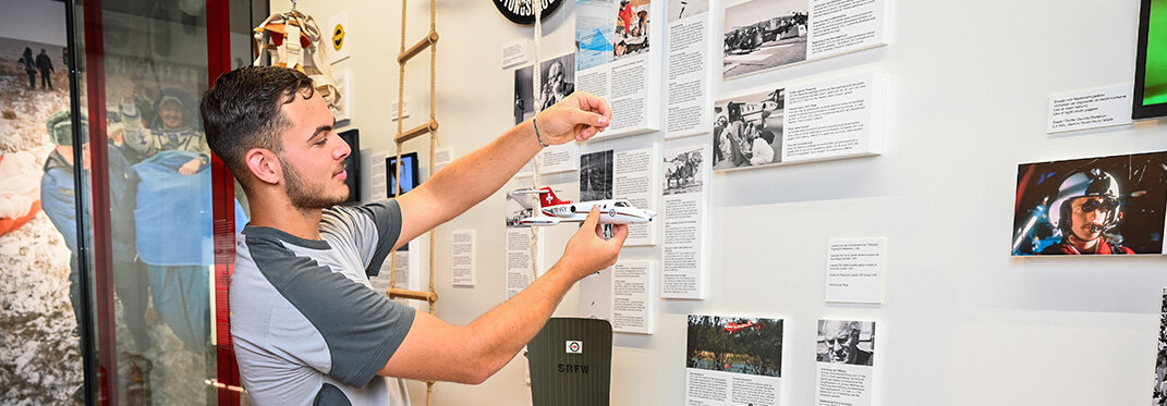 Ein Lehrling hängt ein Modelflugzeug an einem Draht an der Decke auf.