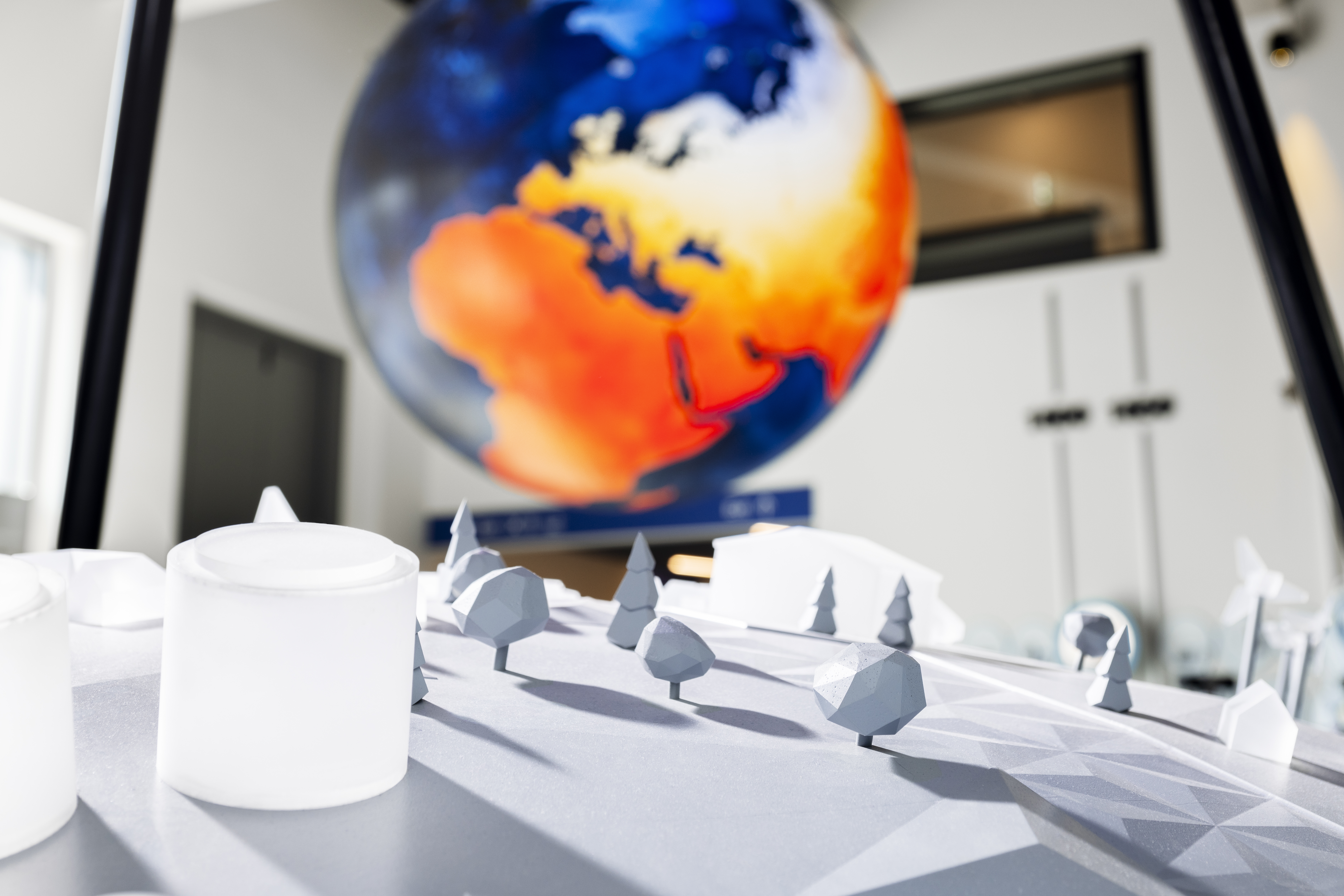 Von der Decke hängt ein großer Globus, der die thermische Signatur anzeigt. Im Vordergrund ist in weiss eine Miniaturlandschaft zu sehen.