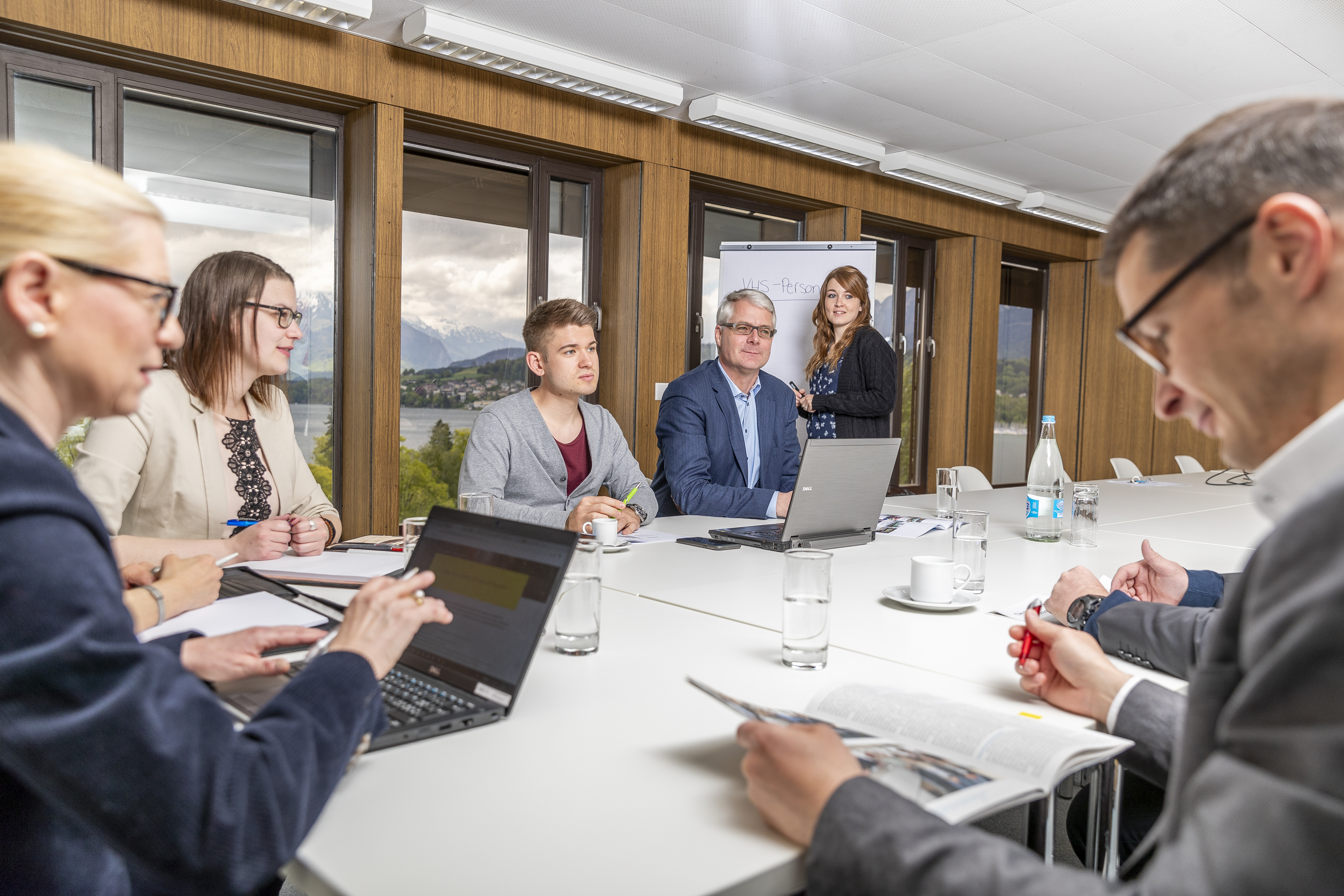 Sechs erwachsene Sitzen an einem Tisch in einem Sitzungszimmer und diskutieren.