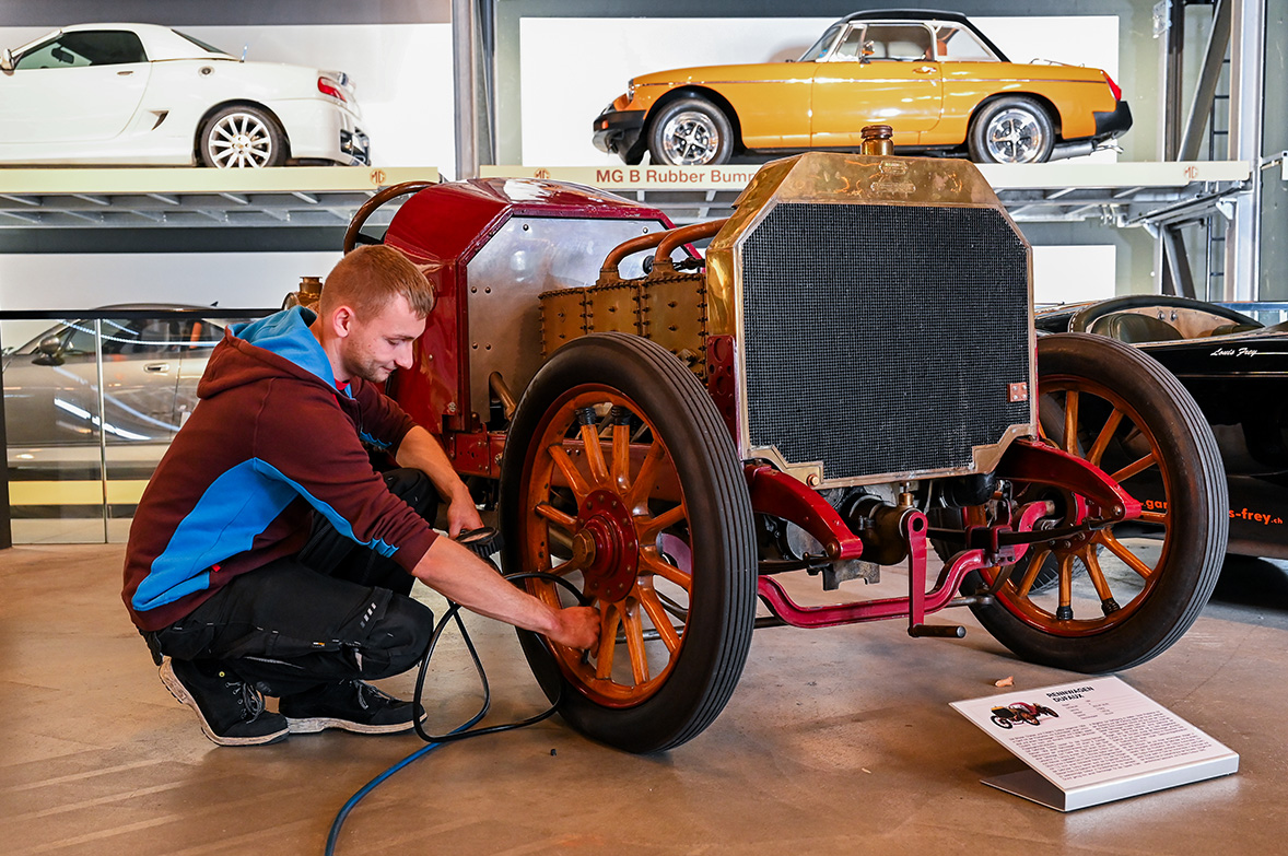 Ein Mann aus dem Zivildienst repariert das Vorderrad eines Oldtimers in einem Automobilausstellung.